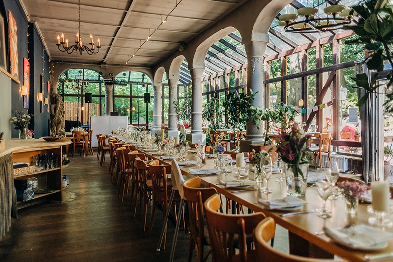 Festlich gedeckter Hochzeitssaal der Zweischlingen in Bielefeld mit langen Tafeln, Blumendekoration und Bogenfenstern.