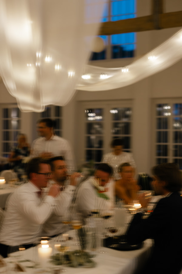 Hochzeitsgäste beim gemeinsamen Dinner an einer langen Tafel im Kerzenlicht